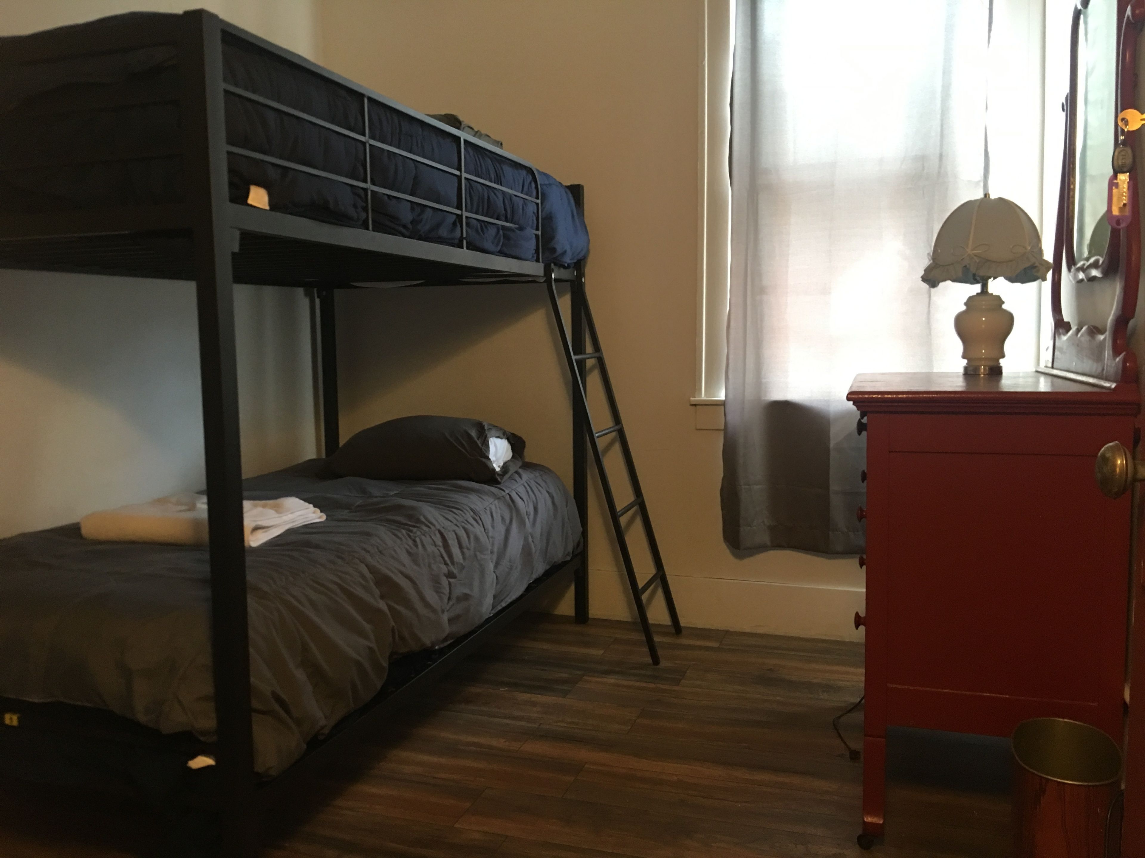Una cama individual superpuesta con escalera, un aparador de madera y una ventana con cortinas.