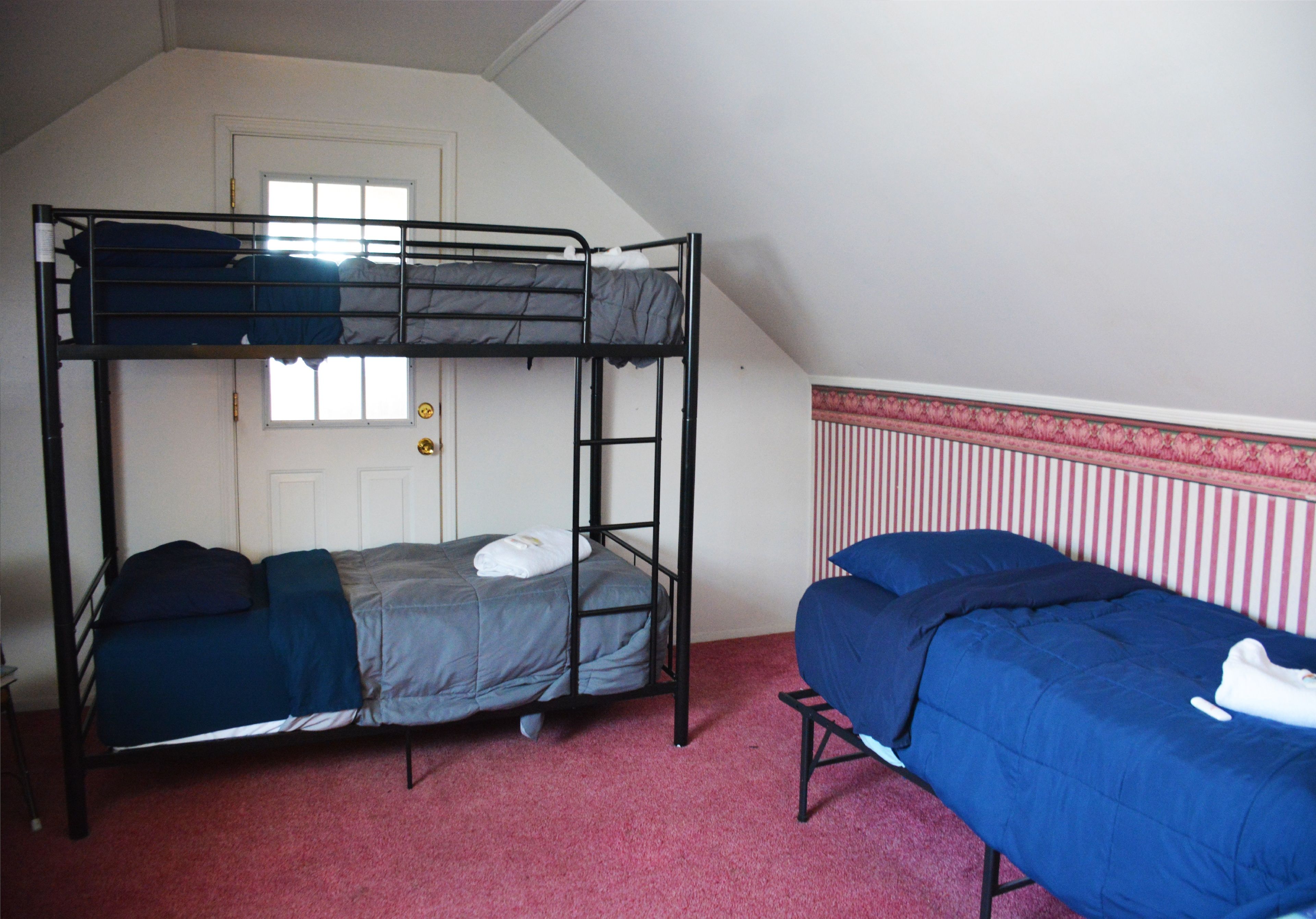 A dormitory room with two bunk beds, a door, and a window.