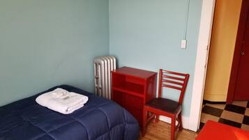 A small room with a bed, a red desk, a chair, a radiator, and a door.