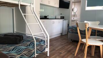 Een kleine kamer met een stapelbed, een kleine kitchenette, een eethoek met tafel en stoelen, en een aan de muur bevestigde televisie.