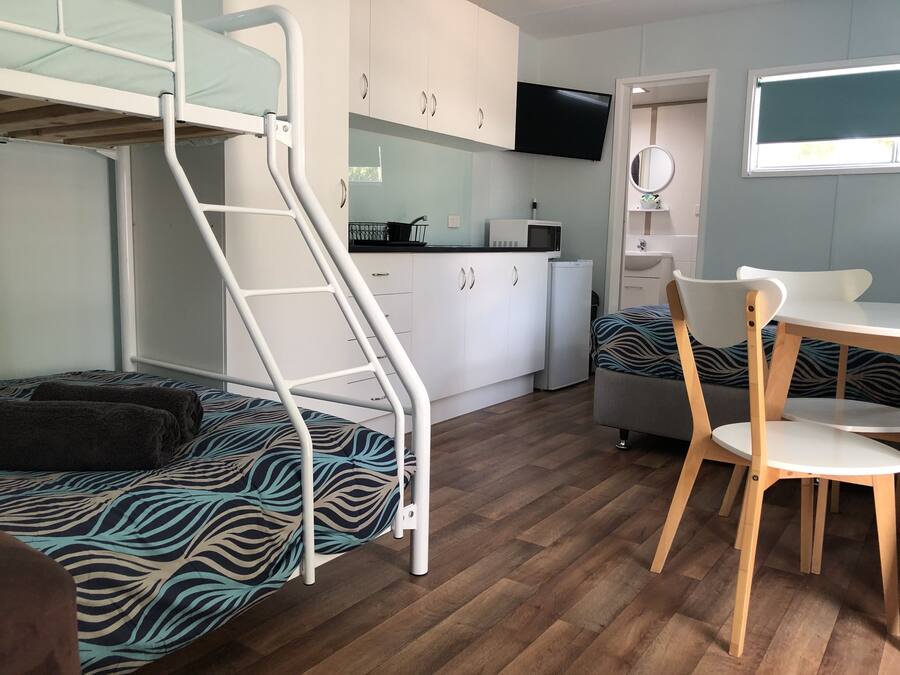 Een kleine kamer met een stapelbed, een kleine kitchenette, een eethoek met tafel en stoelen, en een aan de muur bevestigde televisie.