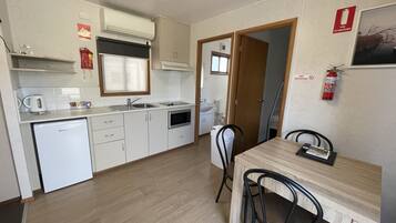 A compact kitchen with white cabinets, a built-in oven, and a microwave. There is a dining table with two chairs and a fire extinguisher mounted on the wall.
