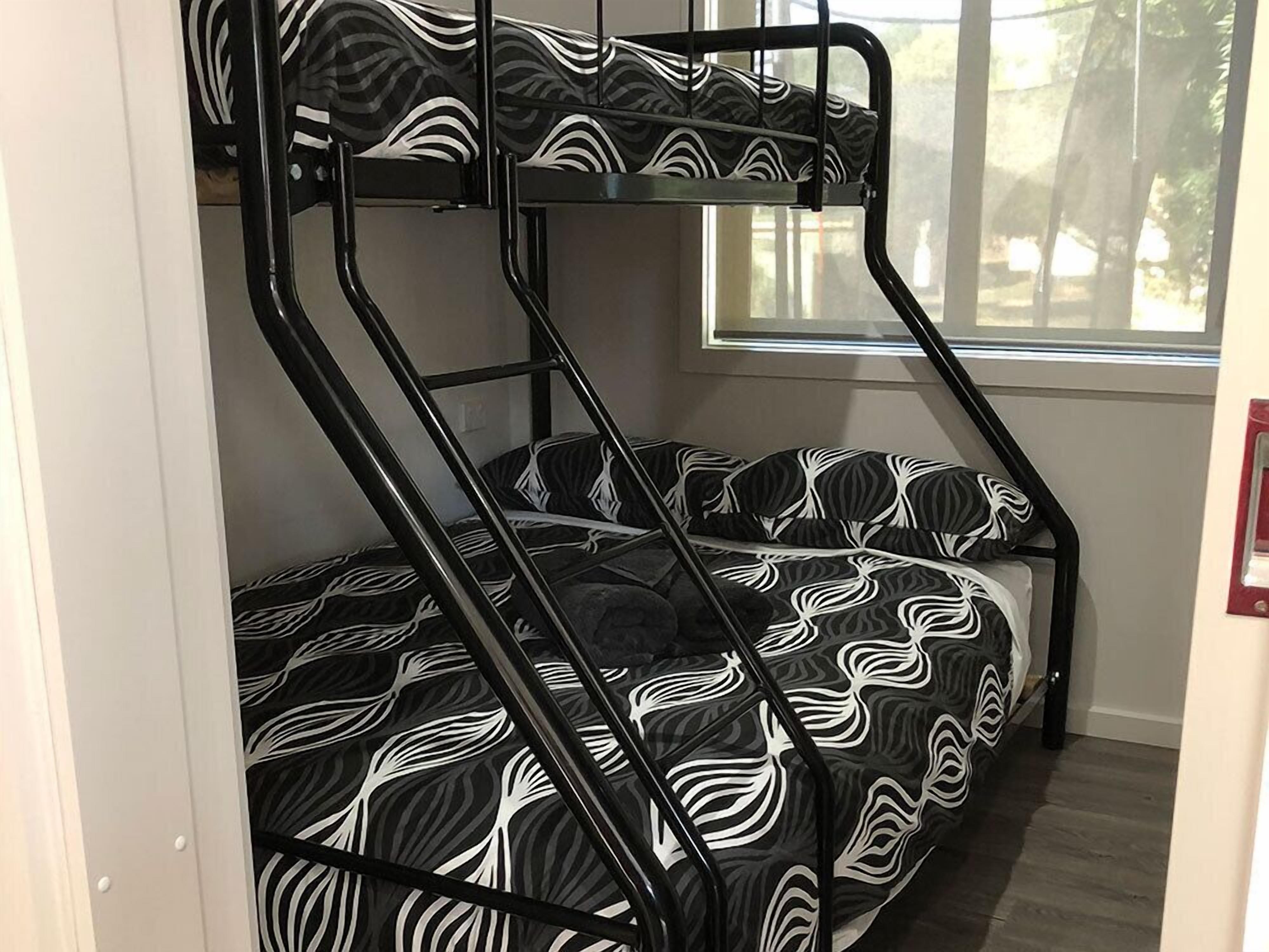 A bunk bed with a black and white patterned mattress, a window with a view of trees, and a door with a red handle.