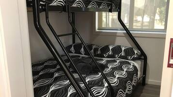 A bunk bed with a black and white patterned mattress, a window with a view of trees, and a door with a red handle.