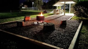 A fire pit with logs, surrounded by gravel, in a park at night. - Acacia Caravan Park (Ararat)