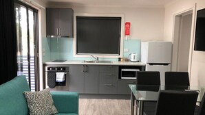 A compact kitchen with a built-in oven, a microwave, and a refrigerator. There is a dining table with chairs and a sofa with a patterned pillow. - Acacia Caravan Park (Ararat)