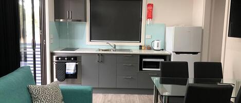 Una cocina compacta con horno integrado, microondas y refrigerador. Hay una mesa de comedor con sillas y un sofá con un cojín estampado.