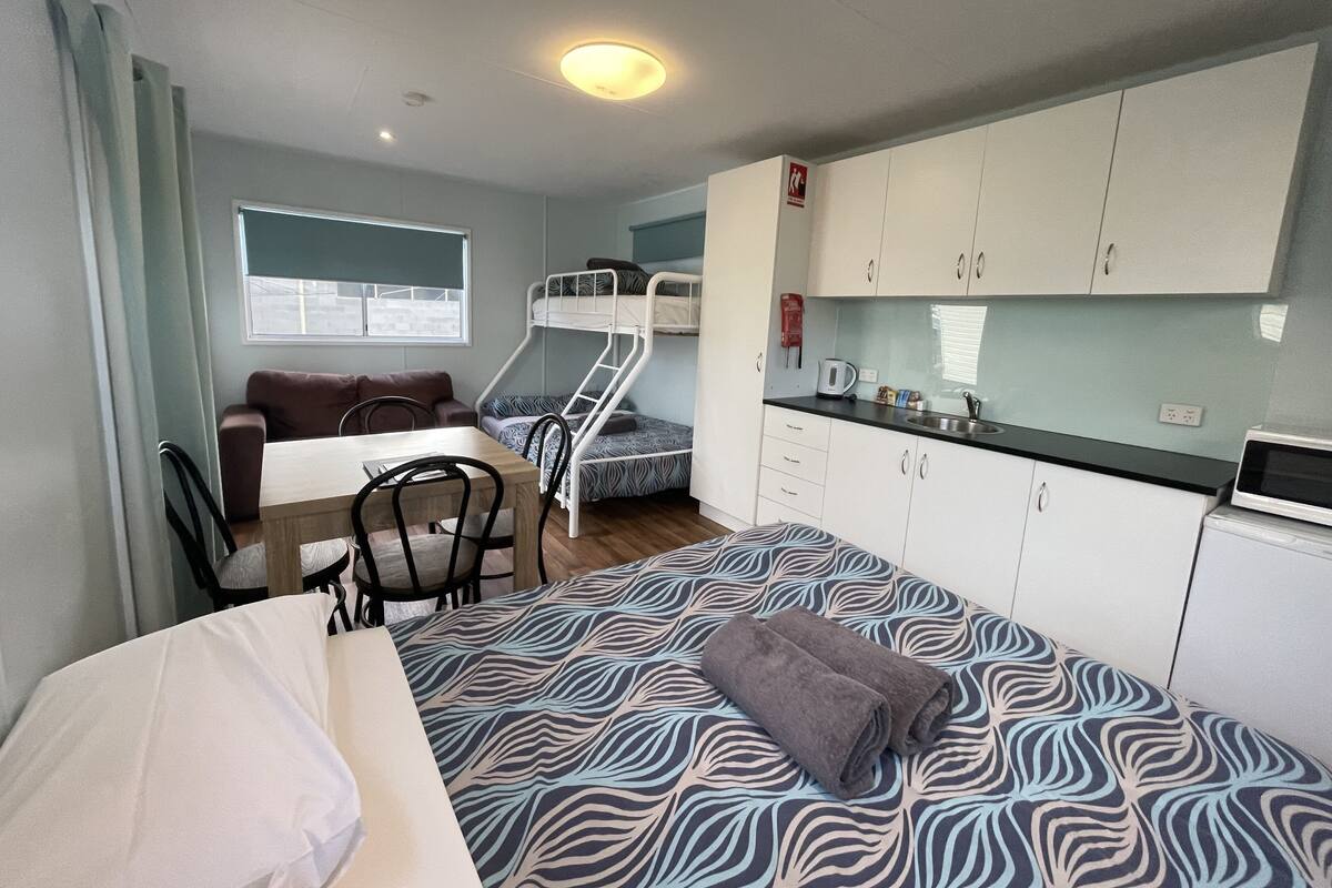Ein kleines Zimmer mit Etagenbetten, einer Küchenzeile, einem Essbereich und einem Sofa.