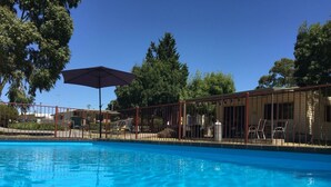 A swimming pool with a clear blue water surface, surrounded by a fenced area with chairs and tables. - Acacia Caravan Park (Ararat)