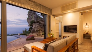 A modern living room with a large TV, comfortable seating, and a view of the ocean. - Hanalee Villa Kouri (Nakijin)