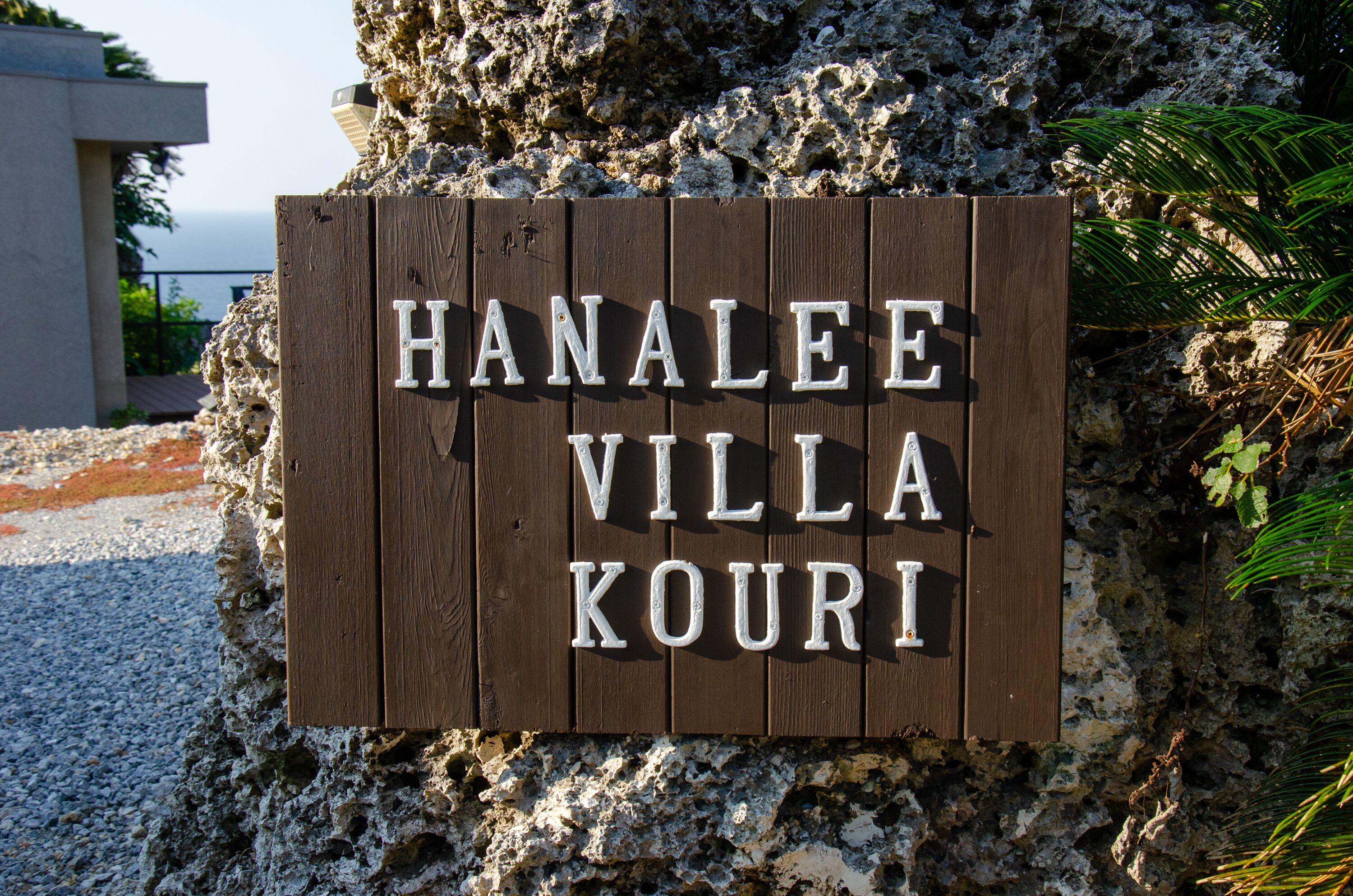 A wooden sign with the text "HanaLEE VILLA KOURI" mounted on a rocky surface.