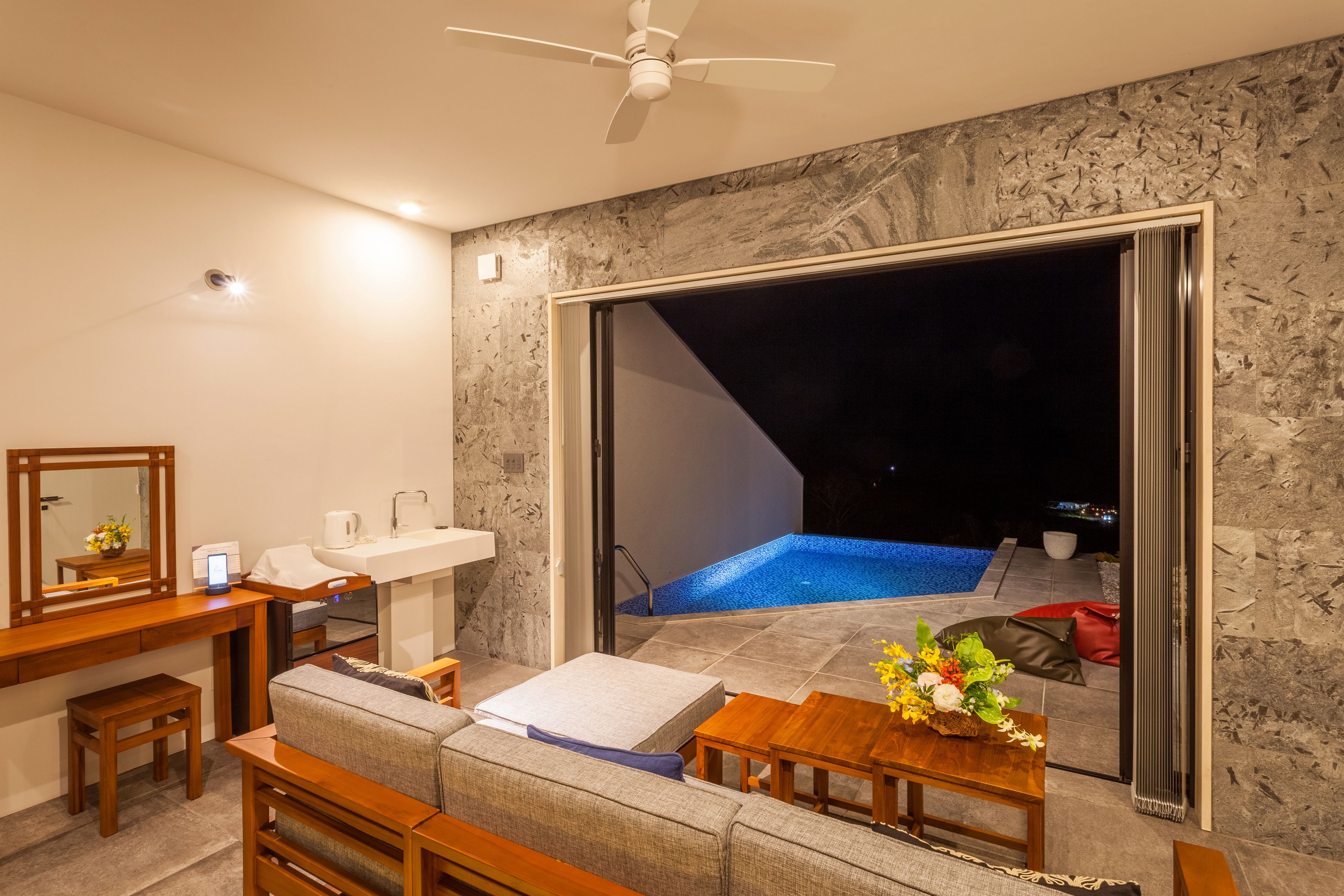 A modern living room with a sofa, coffee table, and a view of an outdoor swimming pool at night.