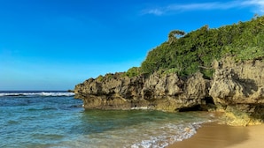 A beach with clear water, a sandy shore, and a rocky cliff with vegetation. - Hanalee Villa Kouri (Nakijin)