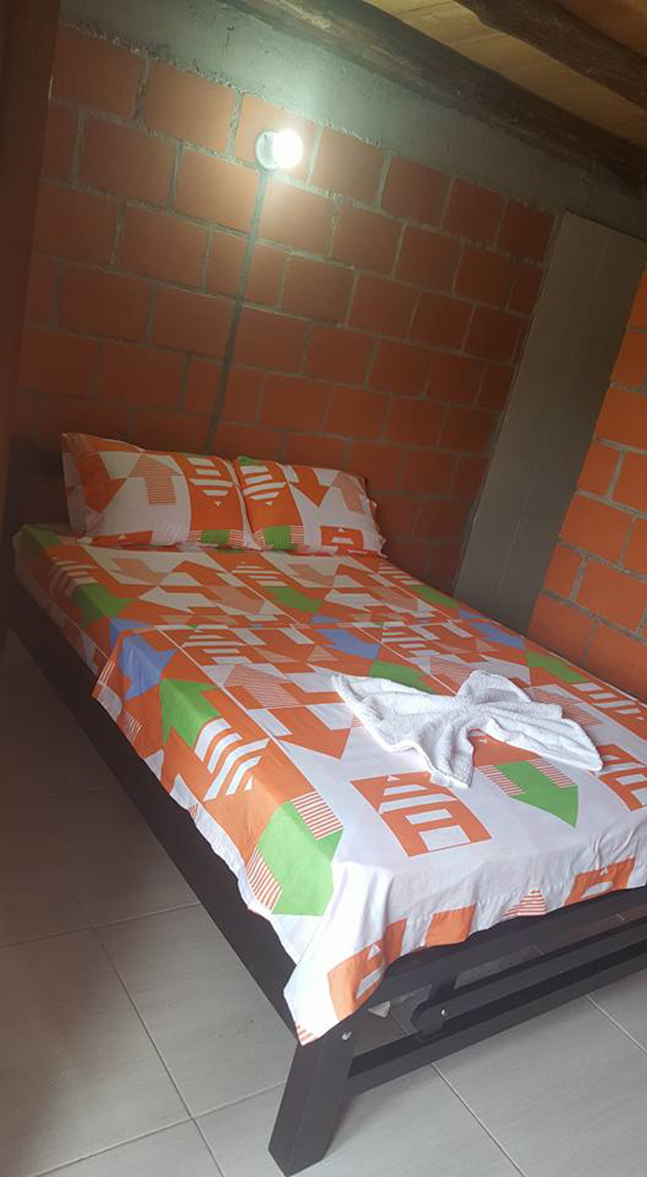 A single bed with a patterned bedspread in a room with brick walls and a tiled floor.