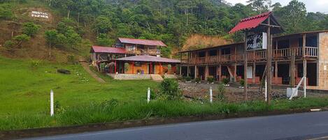 A rustic hotel with a red roof and wooden structure, surrounded by lush greenery and a hillside.