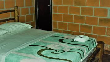 A single bed with a patterned bedspread, a wooden headboard, and a brick wall.