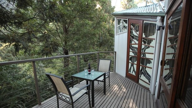 A wooden deck with a table and chairs, overlooking a forested area. - The Lodges (Halls Gap)