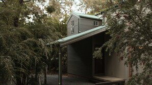 A rustic wooden building with a sloped roof, surrounded by dense foliage. - The Lodges (Halls Gap)