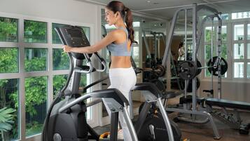 A woman using an elliptical trainer in a gym with large windows and various exercise equipment.