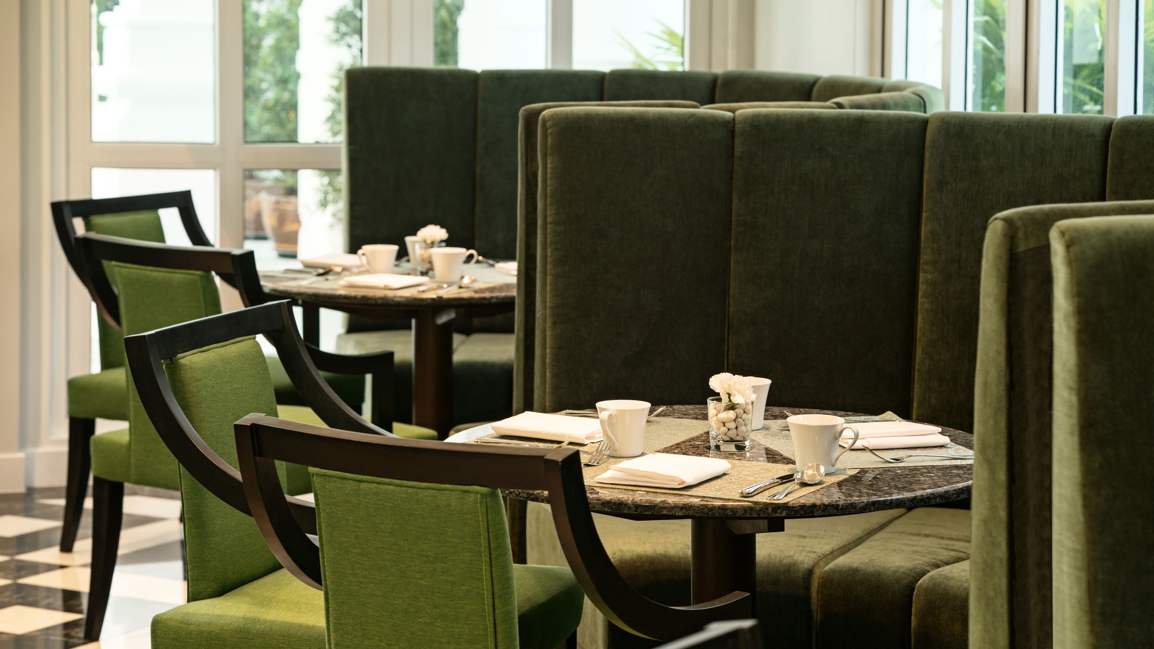 A restaurant with green upholstered booths and tables, each set with white cups and cutlery.