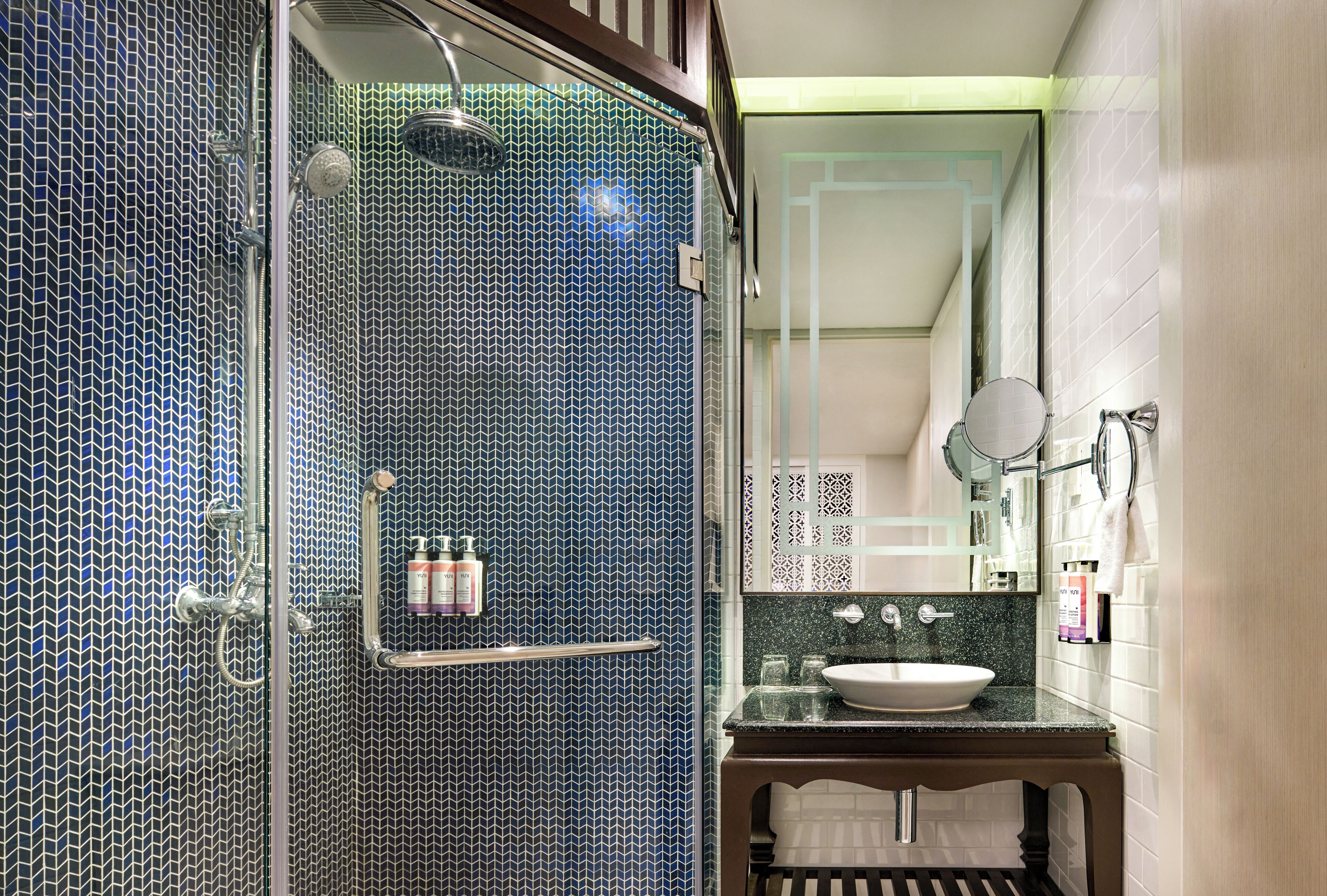 Un baño con zona de ducha con azulejos estampados en azul, un lavabo con encimera de mármol y un espejo encima.
