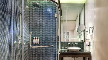 Un baño con zona de ducha con azulejos estampados en azul, un lavabo con encimera de mármol y un espejo encima.