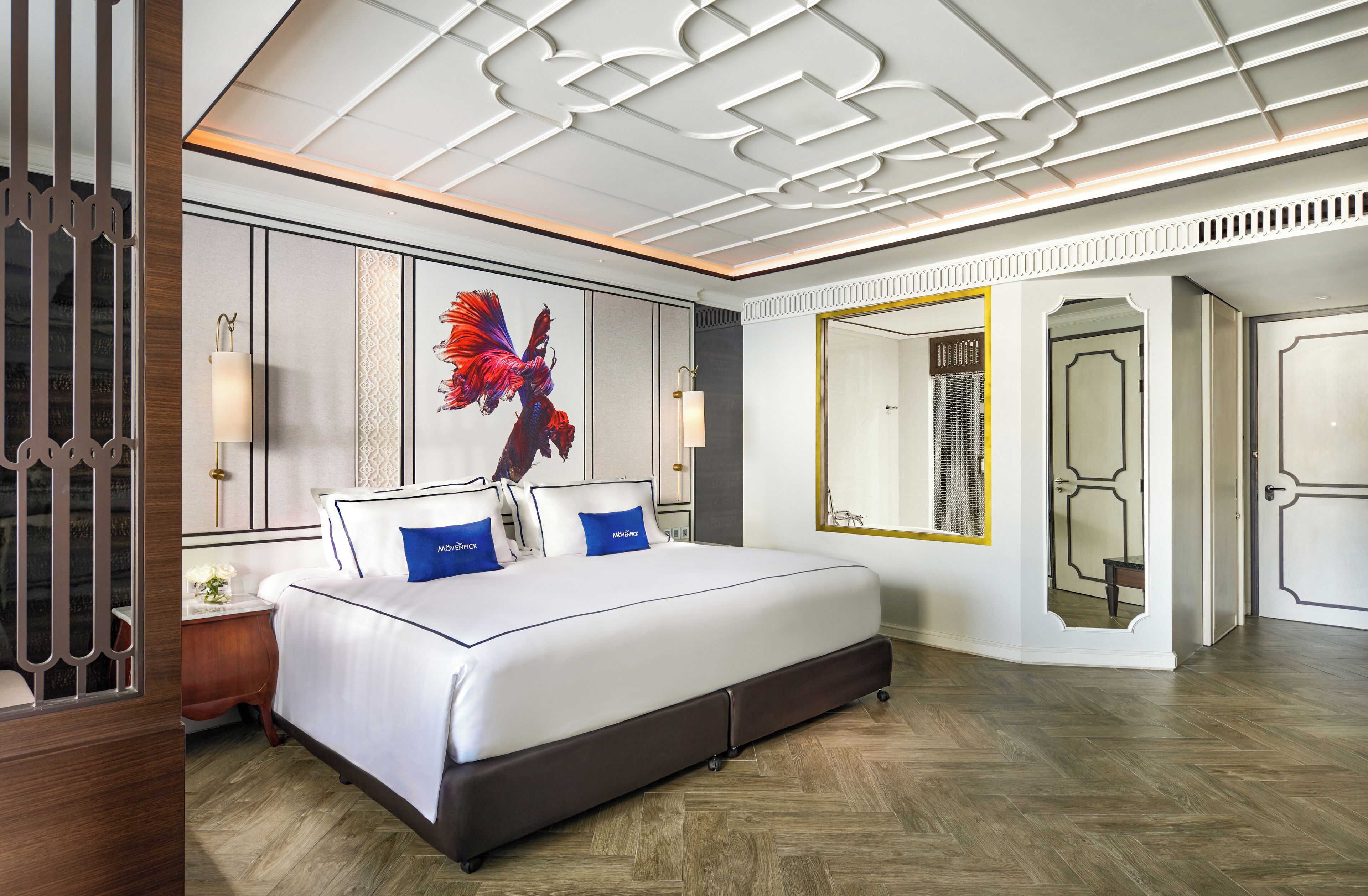 A modern hotel room with a large bed, decorative ceiling, and a mirror with a gold frame.