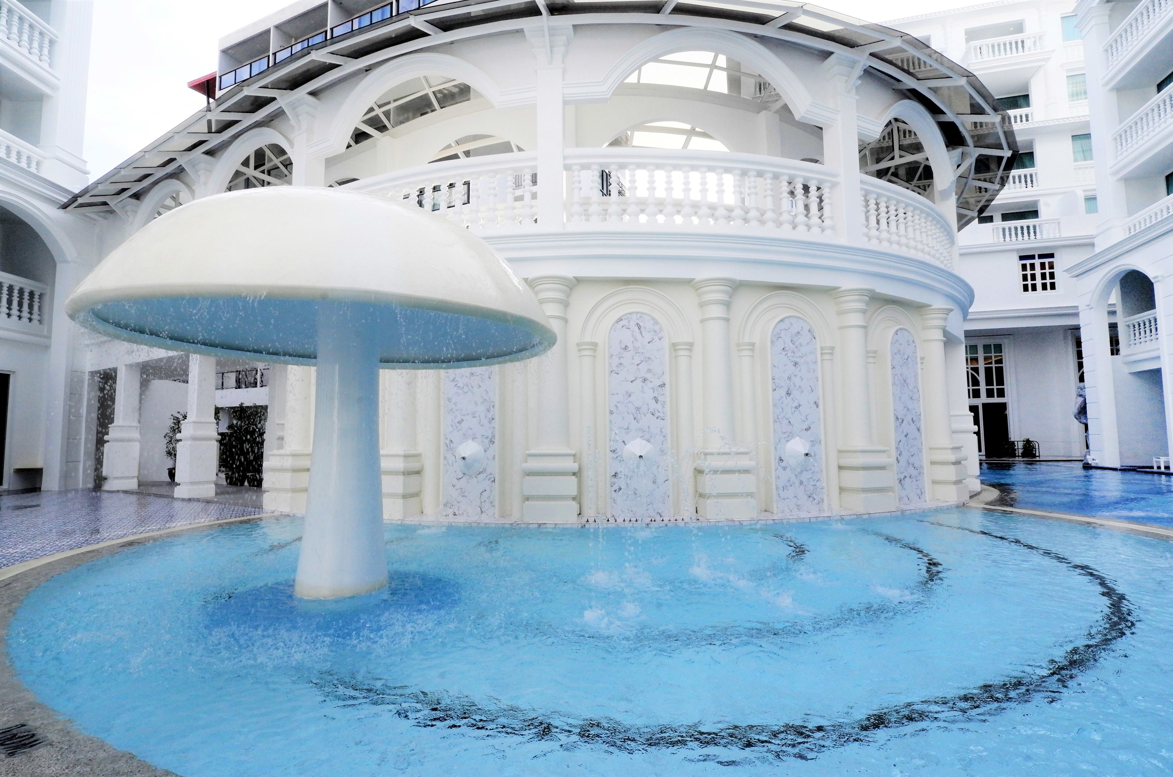 A spacious atrium with a large fountain, white marble columns, and a grand staircase.