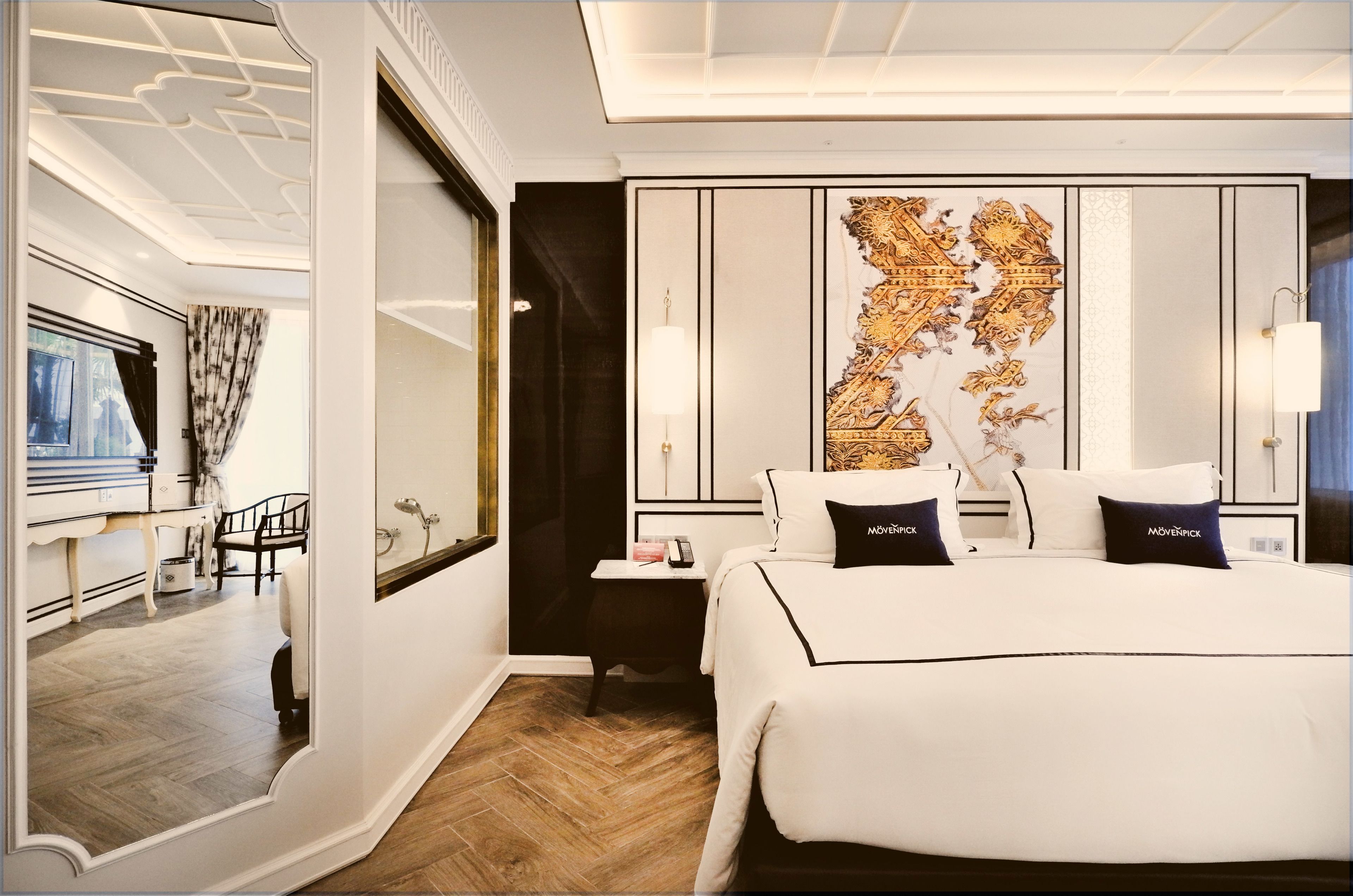 A modern hotel room with a large bed, a decorative wall panel, a bedside table, and a mirror.