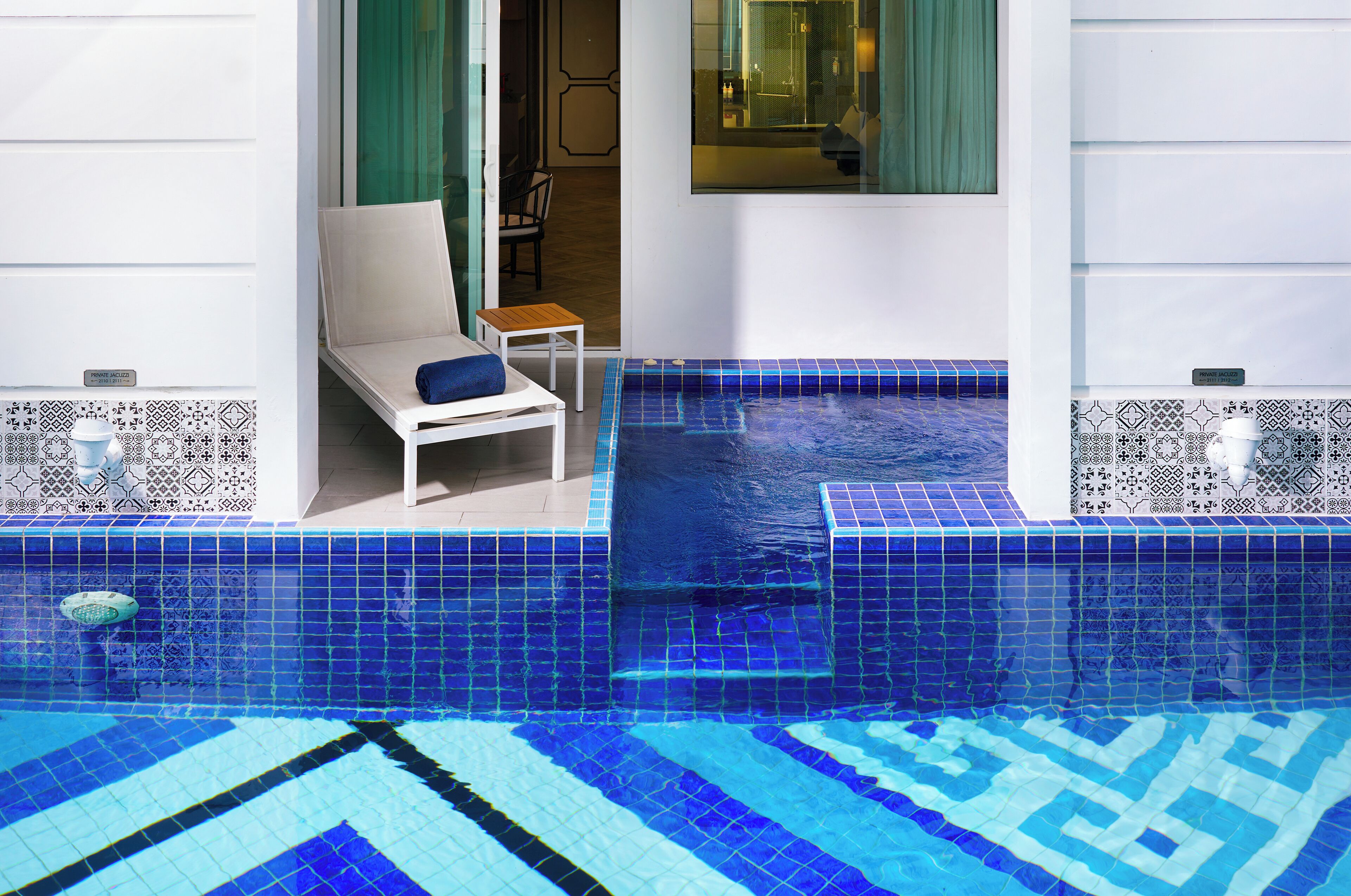 Un espace piscine doté d’un sol carrelé de carreaux bleus, d’une chaise longue et d’une petite table.