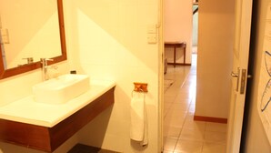 A bathroom with a sink, mirror, towel rack, and a door leading to another room.