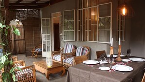 A dining area with a table set for four, surrounded by wicker chairs, a wooden table, and a large window with blinds.