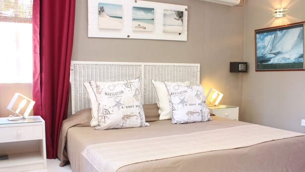 A neatly made bed with two pillows, a bedside table with a lamp, and a wall with framed pictures.