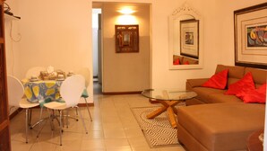 A living room with a brown sofa, a glass coffee table, and a dining area with a table set for four.