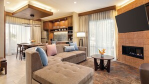 A modern living room with a sectional sofa, a fireplace, a flat-screen TV, and a kitchen area in the background. - Hoodoo Moab, Curio Collection by Hilton (Moab)