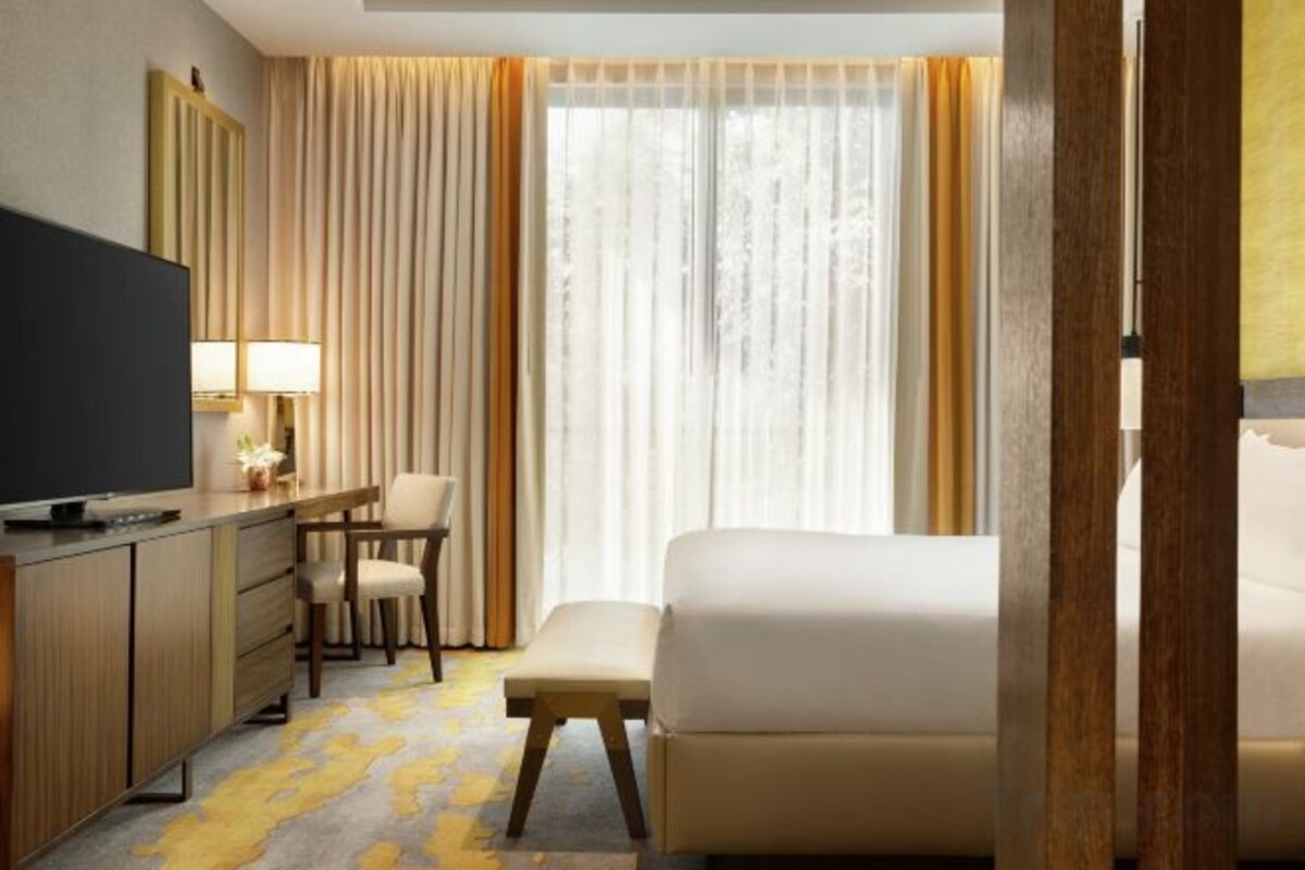A hotel room with a bed, a desk with a television, a chair, and a window with curtains.