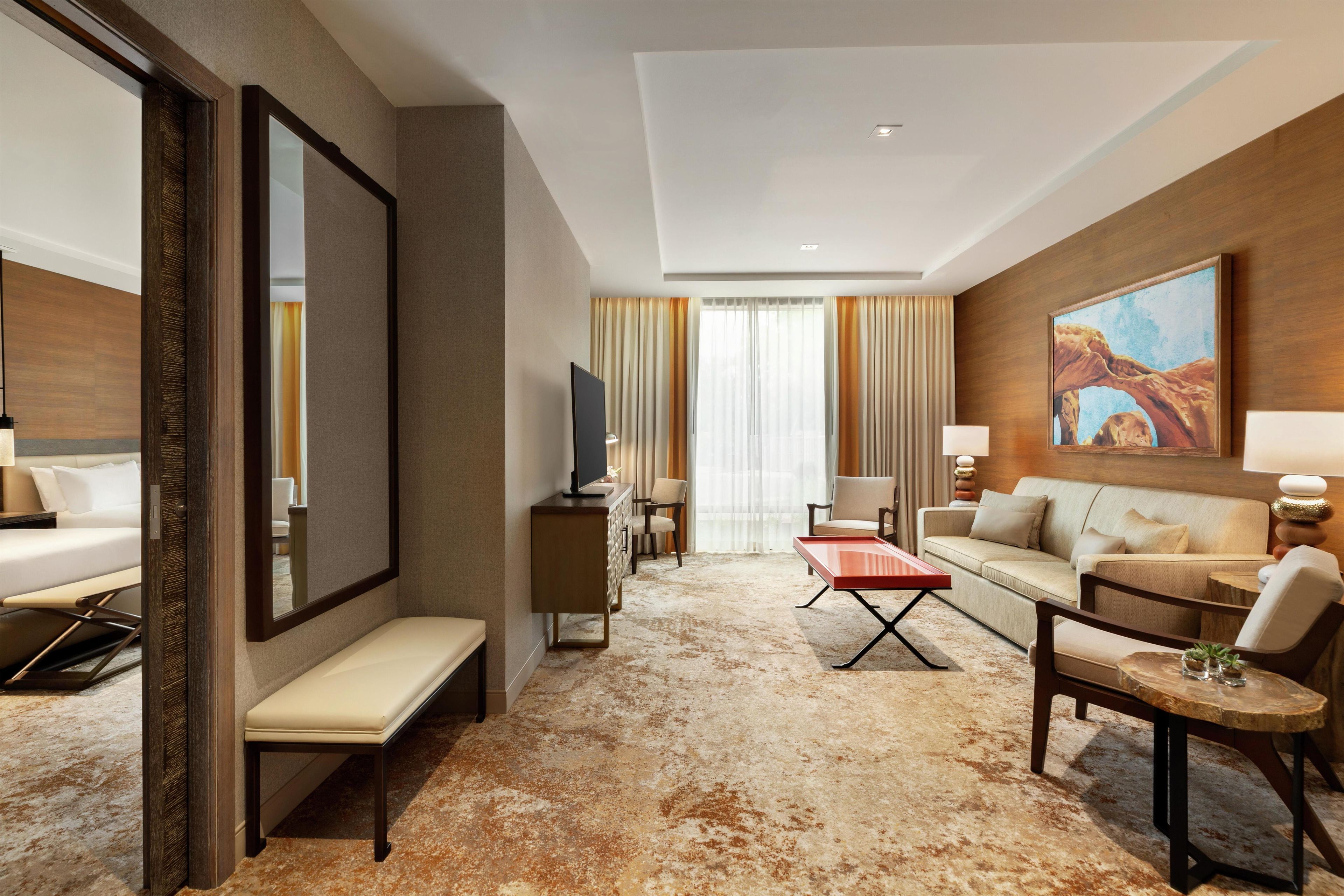 A hotel room with a bed, a sofa, a coffee table, a TV, and a painting on the wall.