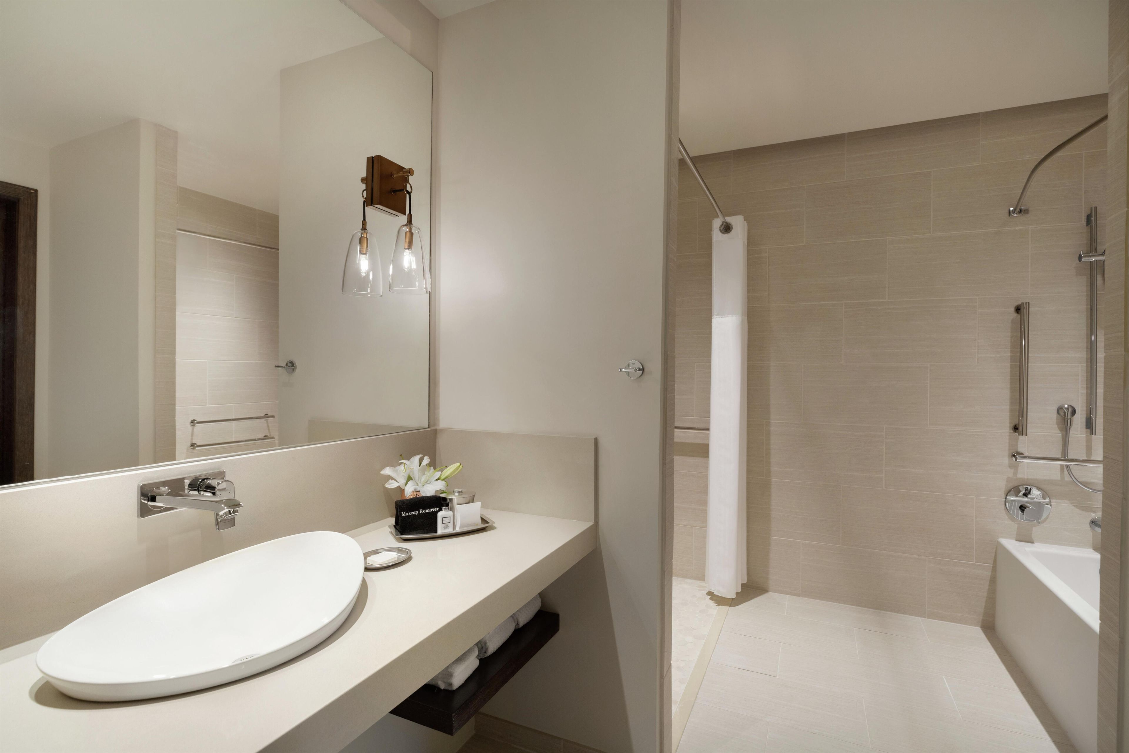 Ein modernes Badezimmer mit großem Spiegel, rundem Waschbecken, einer Dusche mit Glastür und einem Handtuchhalter.