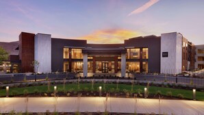 A modern hotel with a central entrance, large windows, and a landscaped garden area. - Hoodoo Moab, Curio Collection by Hilton (Moab)