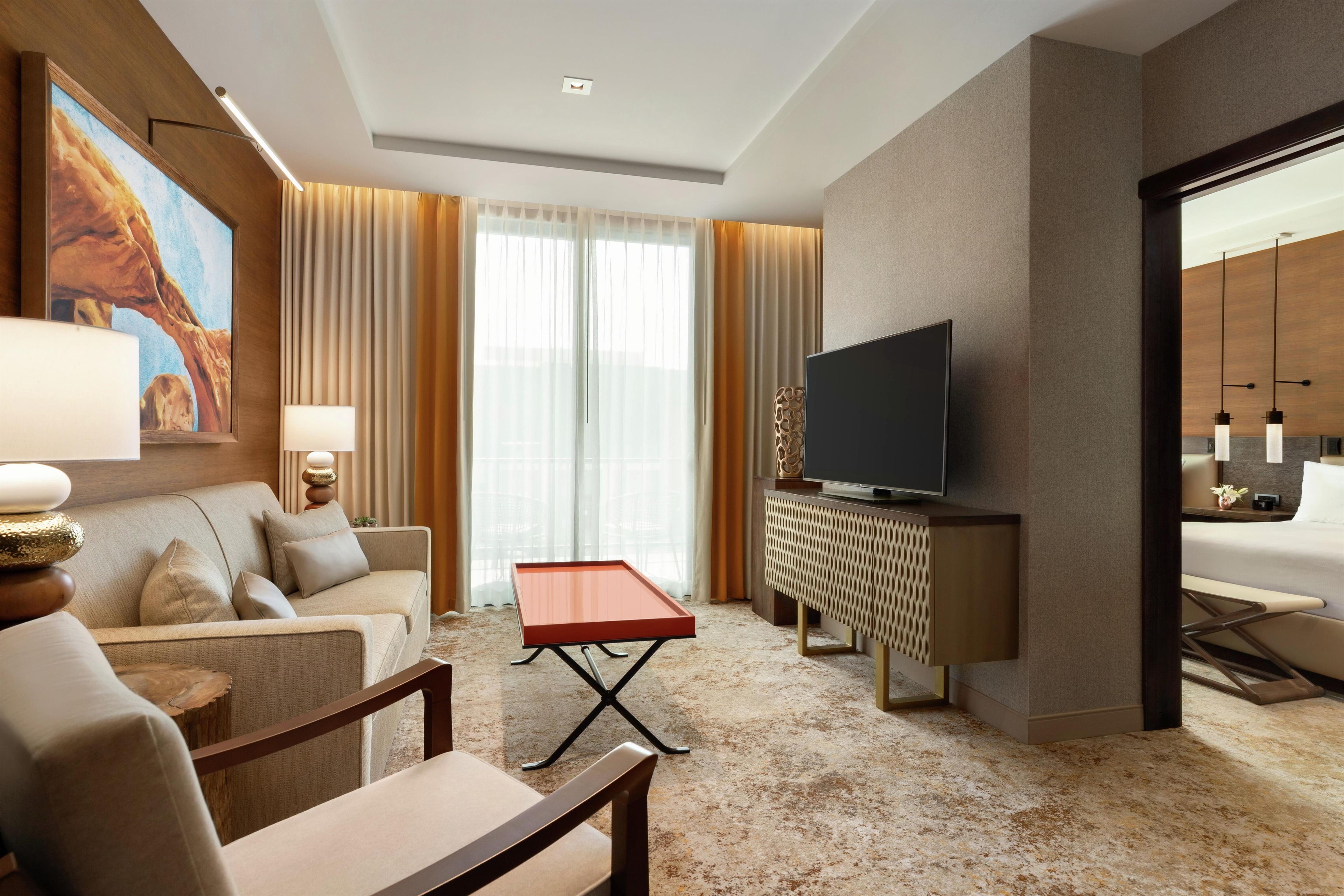 Una habitación de hotel con sofá, una mesita, televisor y una lámpara decorativa.