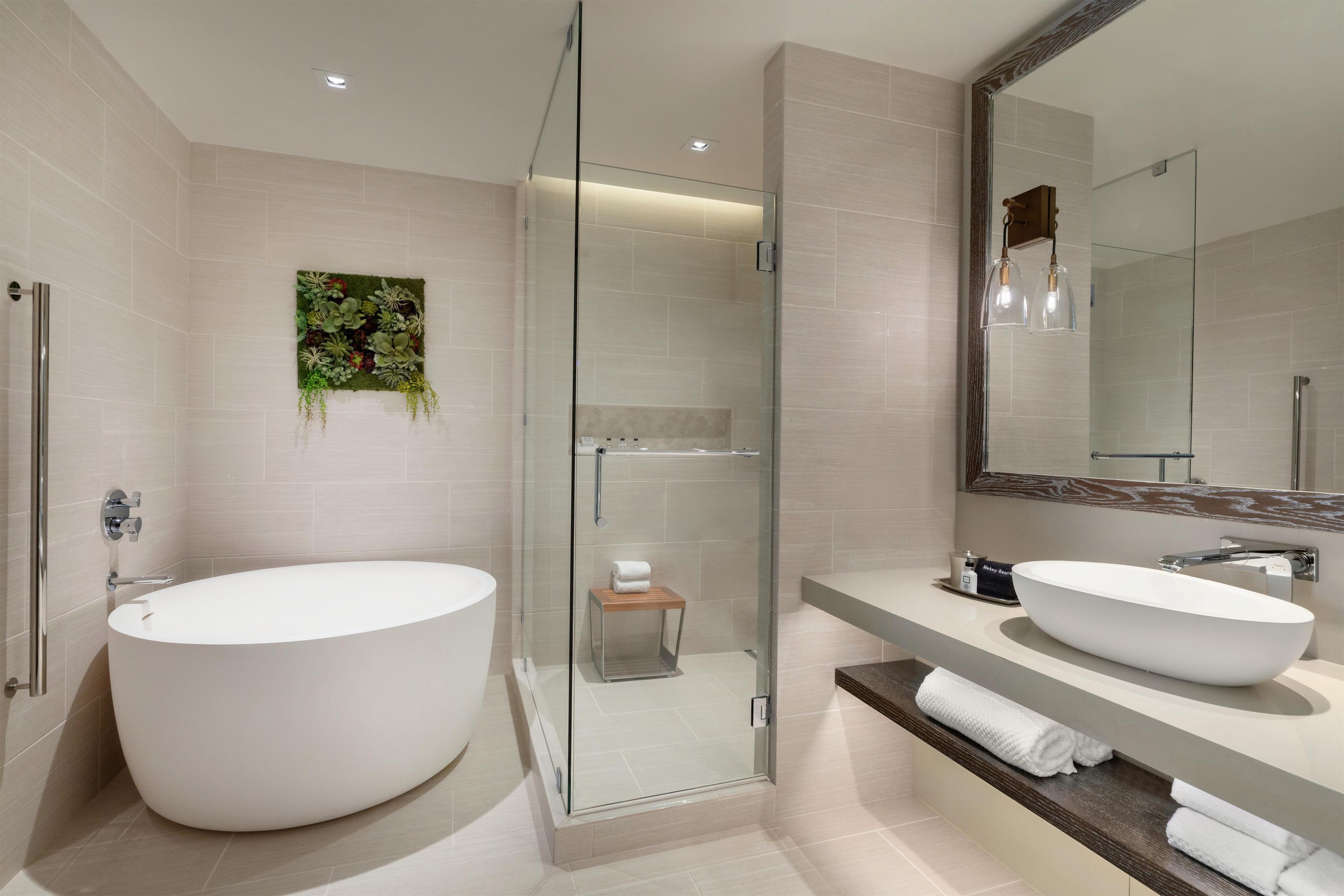 Une salle de bain moderne dotée d’une grande baignoire sur pieds, de deux vasques, d’une douche à parois de verre et d’un miroir avec un cadre décoratif.