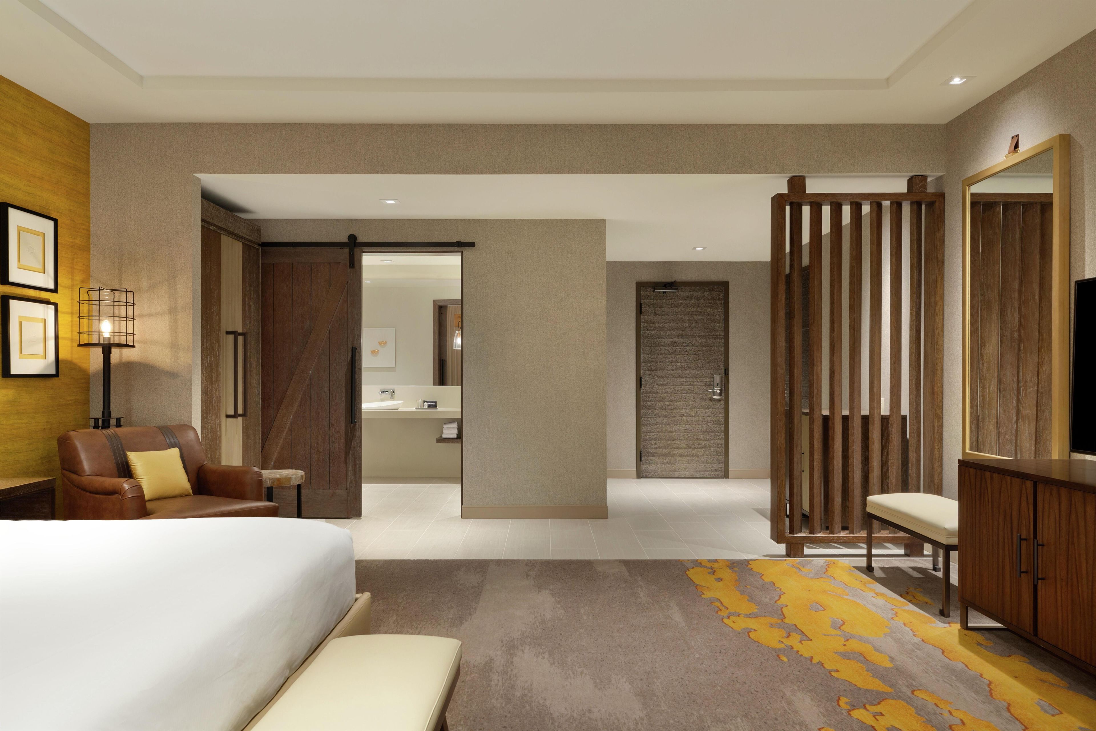 Une chambre d’hôtel comprenant un lit, un bureau, une chaise, un canapé, une télévision, une salle de bain et un mur décoratif.
