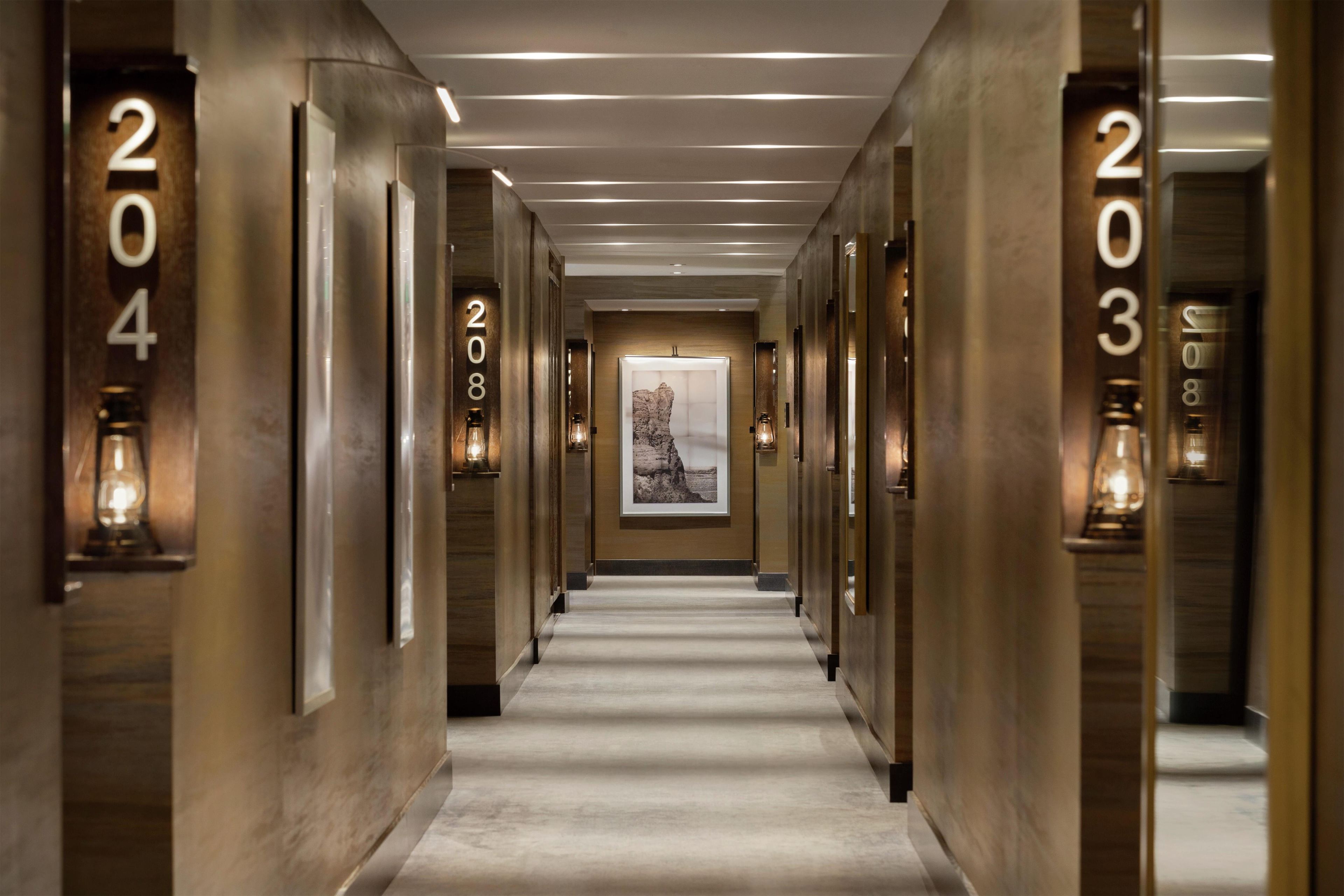 A hotel hallway with numbered doors, a framed picture on the wall, and a carpeted floor.