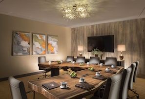 A conference room with a large wooden table, multiple chairs, a television, and two wall-mounted lamps.