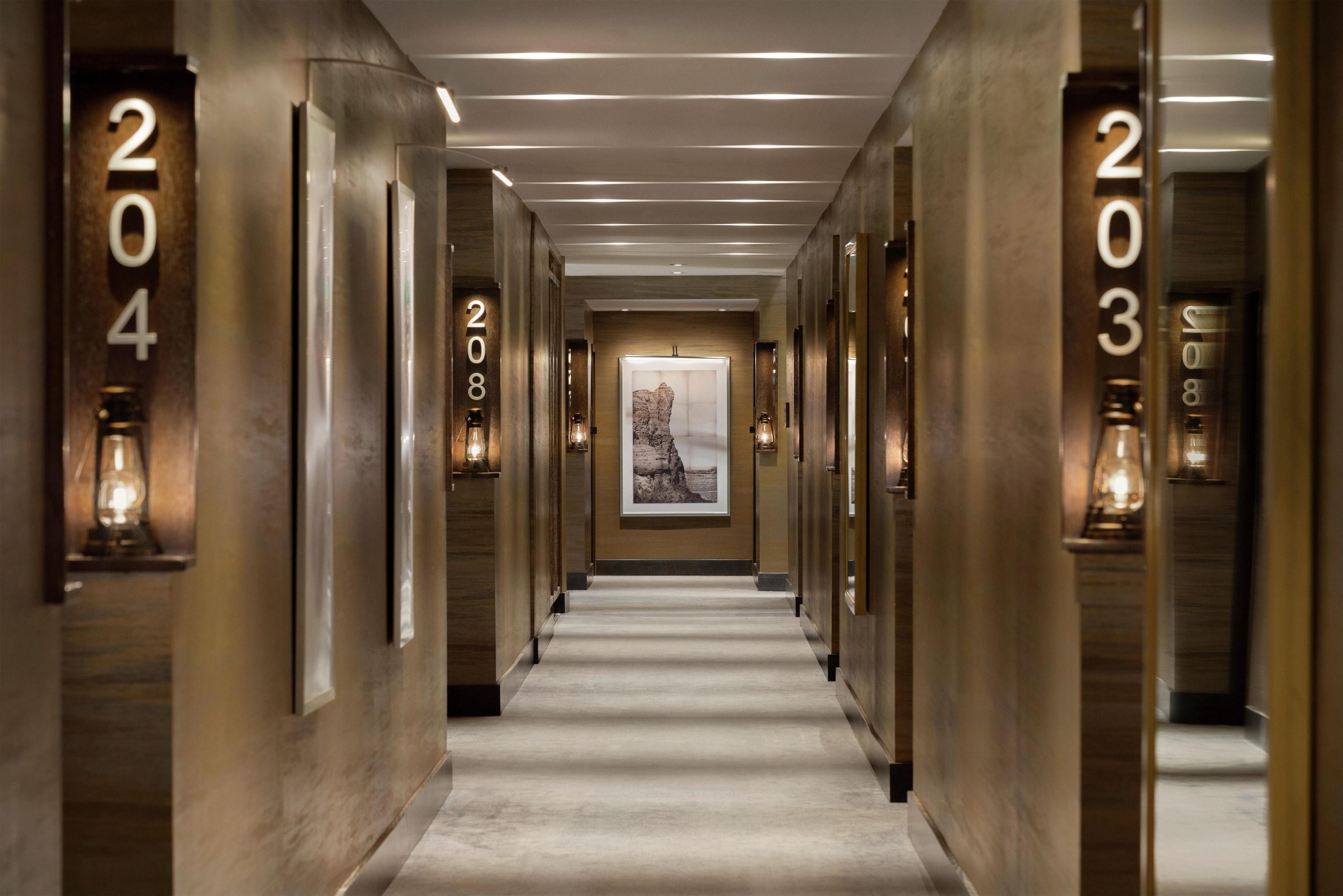 A hotel hallway with numbered doors, a framed picture on the wall, and a carpeted floor.
