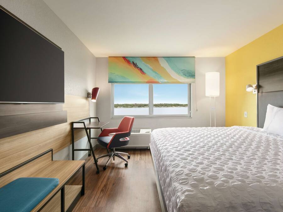 A hotel room with a bed, desk, chair, and a large window with a view.