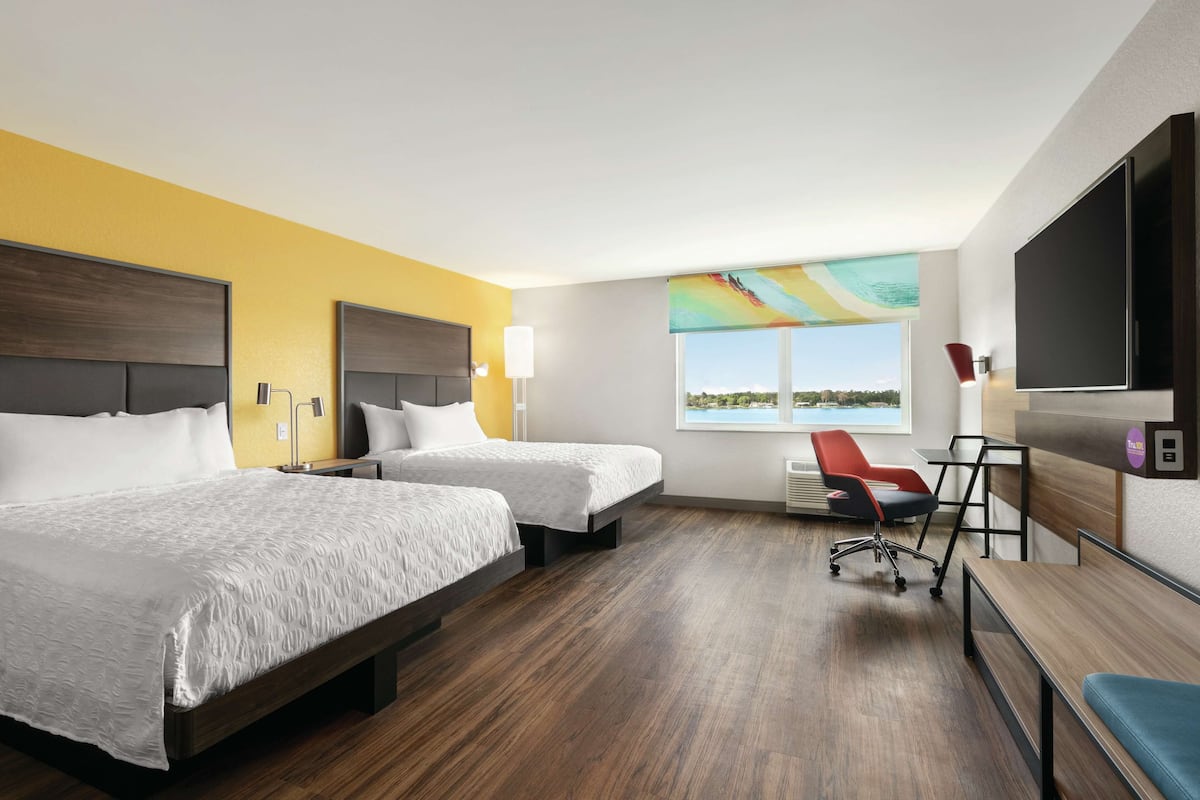 Habitación de hotel con dos camas, un escritorio, una silla, un televisor y ventana con vista.