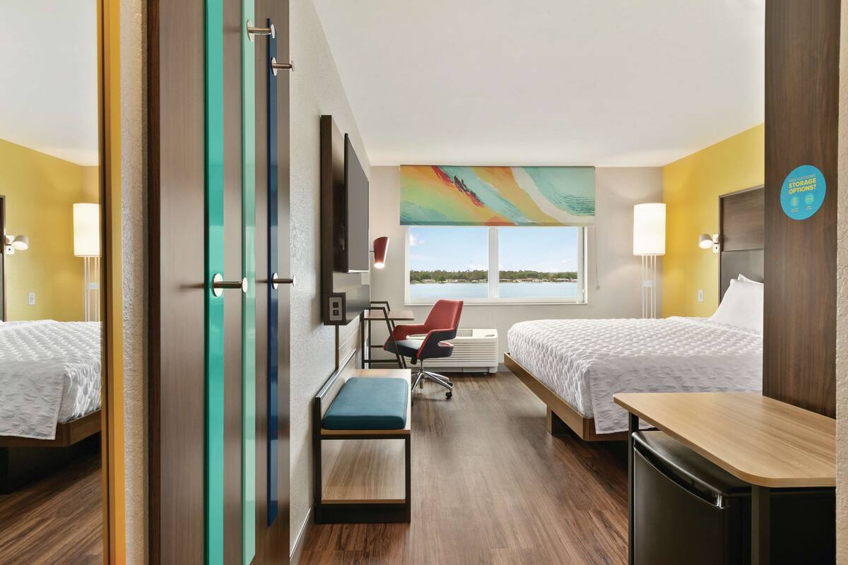 A hotel room with two beds, a desk, a chair, and a large window with a view.