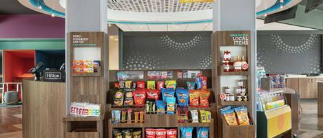 Kiosco de mercado abierto las 24 horas, con aperitivos y bebidas, un letrero que dice 'comer y beber' y un letrero que invita a 'descubrir nuestros productos locales'.