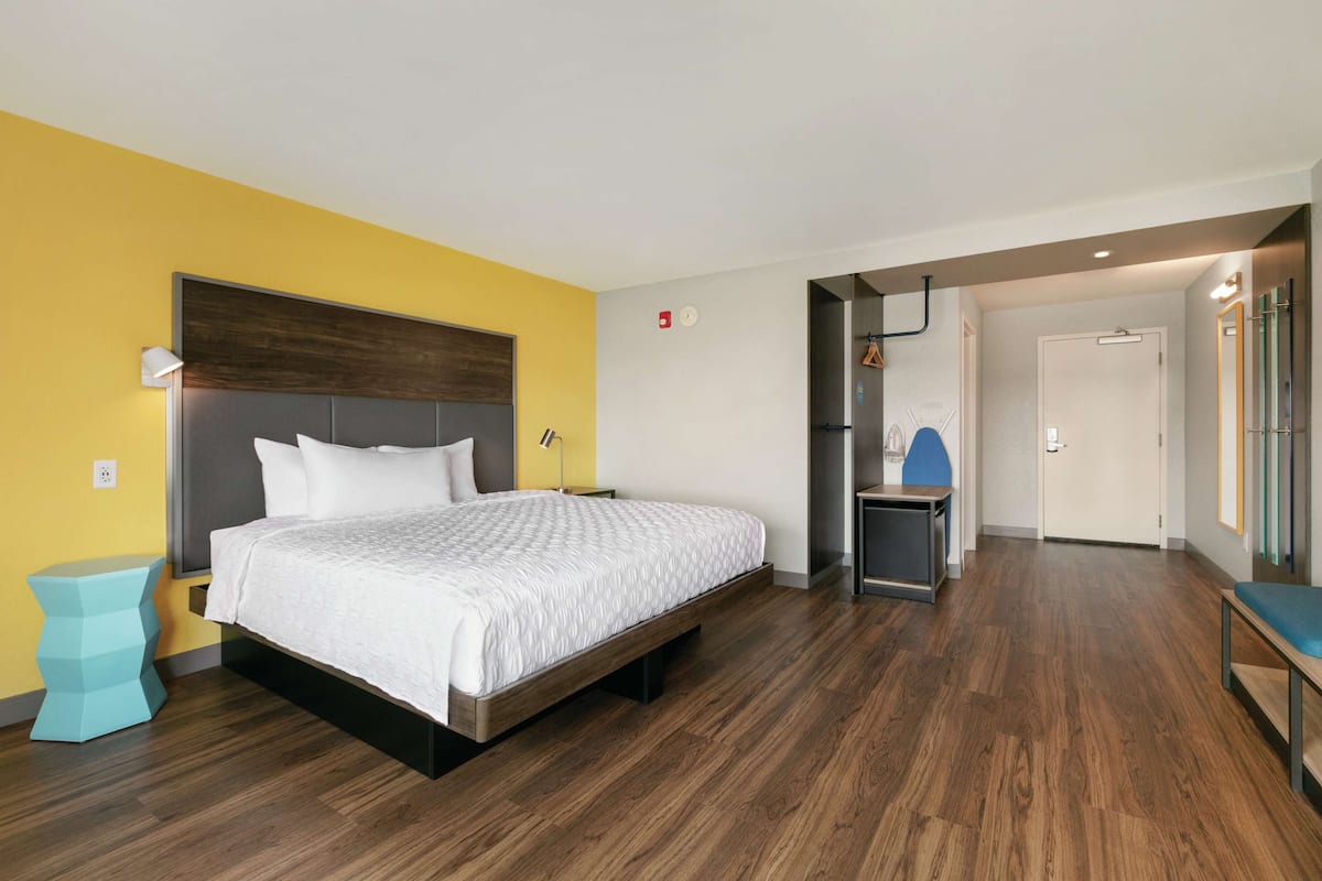 A modern hotel room with a wooden floor, a bed with white bedding, a small side table, and a bench.